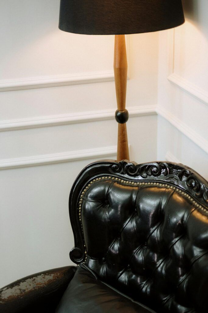 A classic interior with a black leather armchair and vintage lamp against white paneling, exuding elegance.