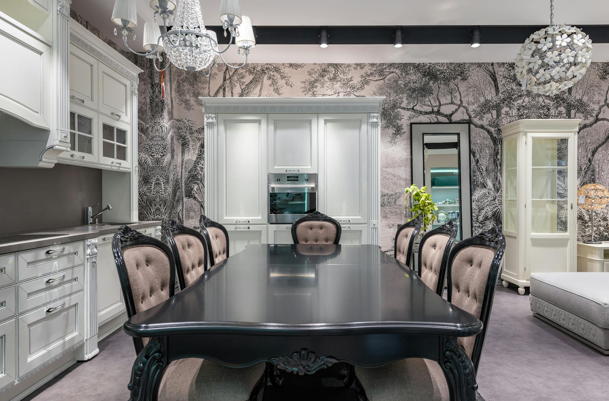 Black table with chairs placed near white cupboards and modern appliances in stylish spacious kitchen with mirror and creative wallpaper