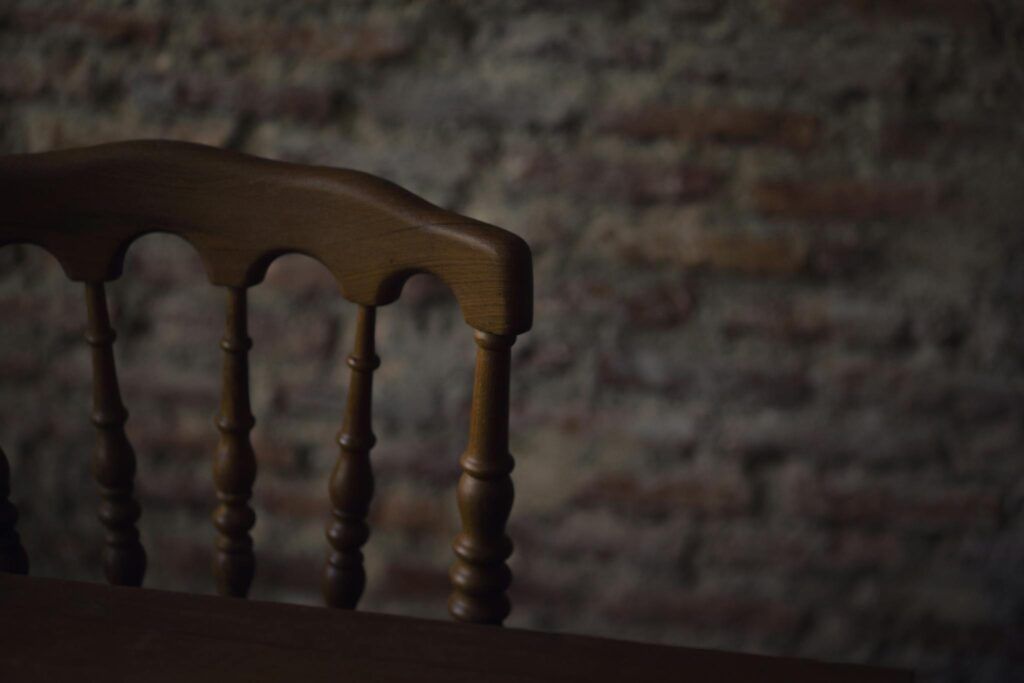 Close-up of an antique wooden chair with a textured, rustic brick wall background.